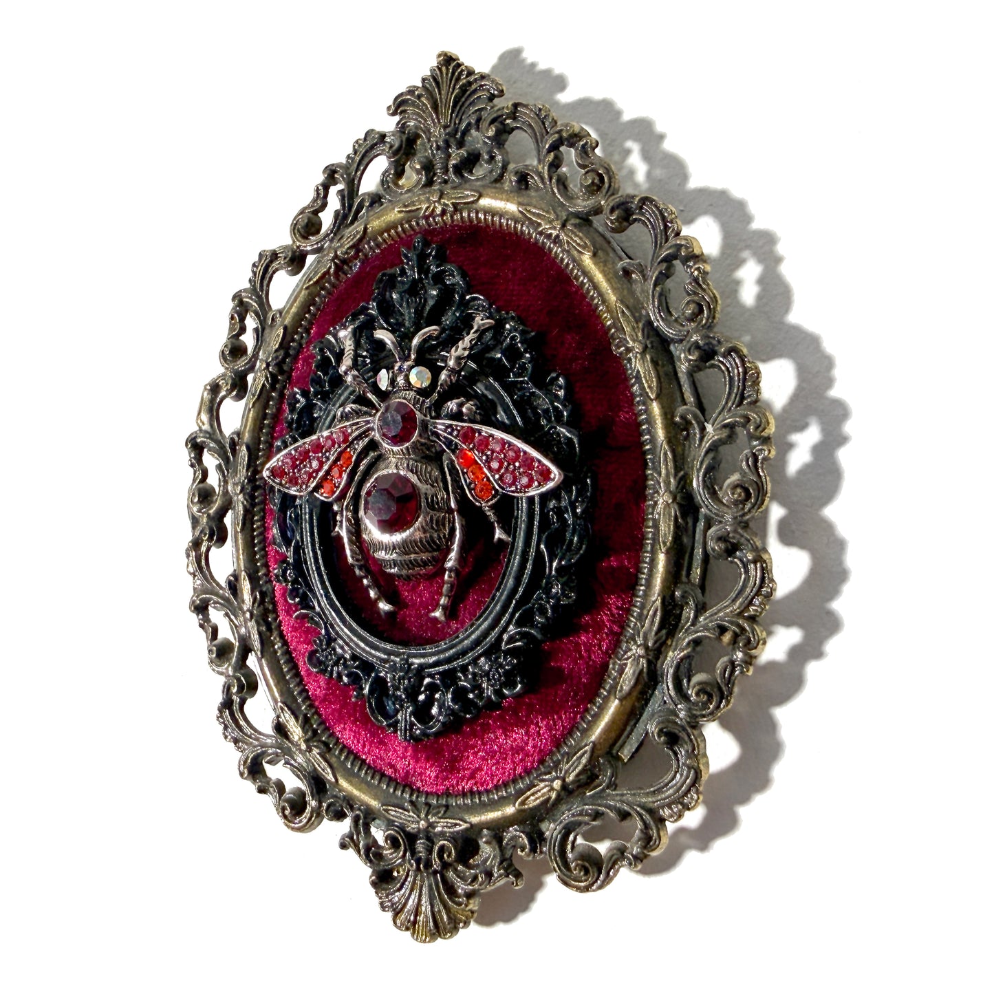 Decorative antique frame with silver bee on red velvet in an ornate frame.