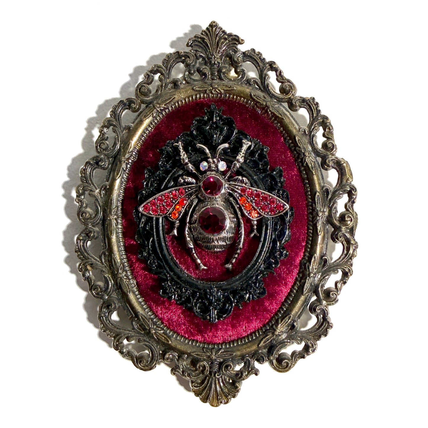 Decorative antique frame with silver bee on red velvet in an ornate frame.
