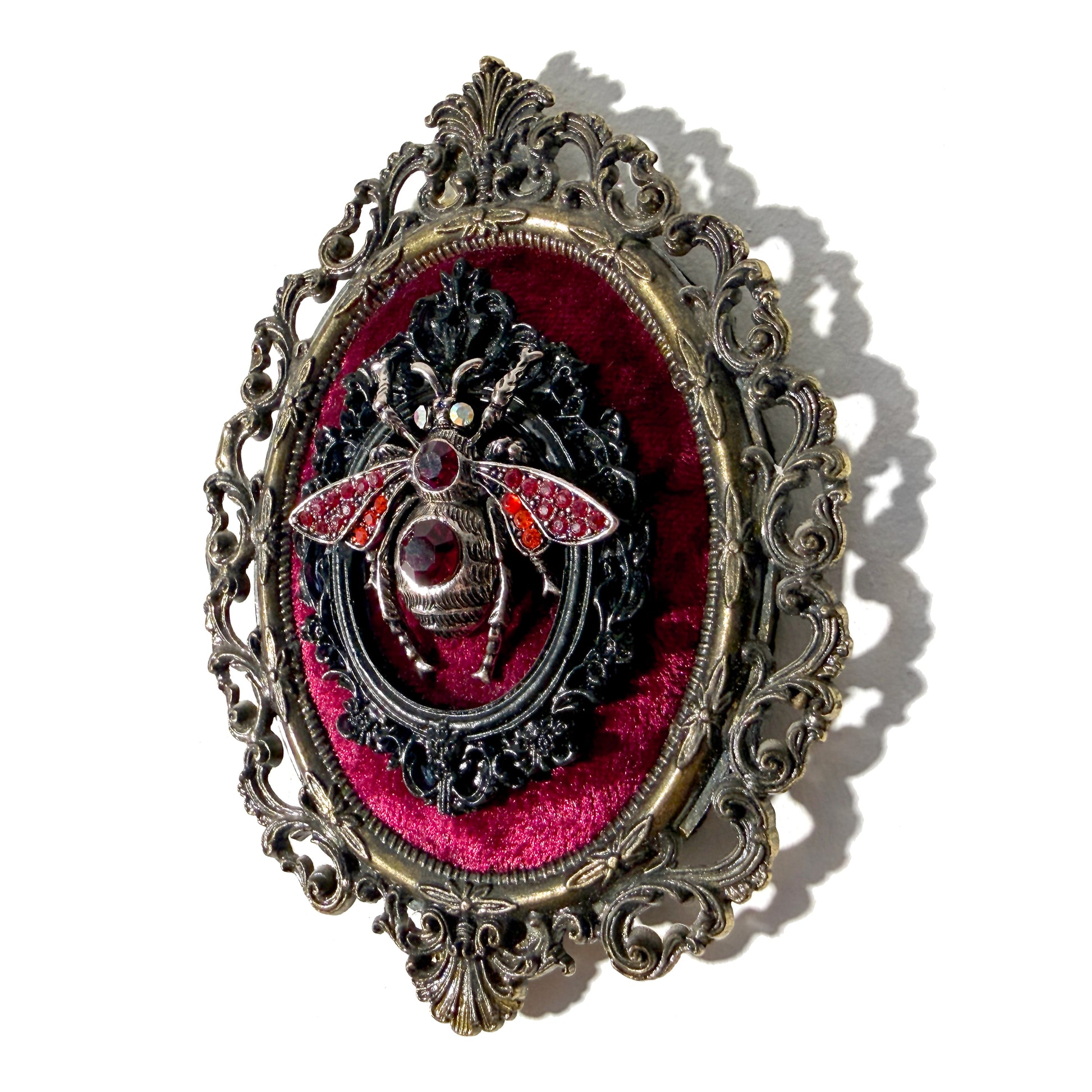 Decorative antique frame with silver bee on red velvet in an ornate frame.